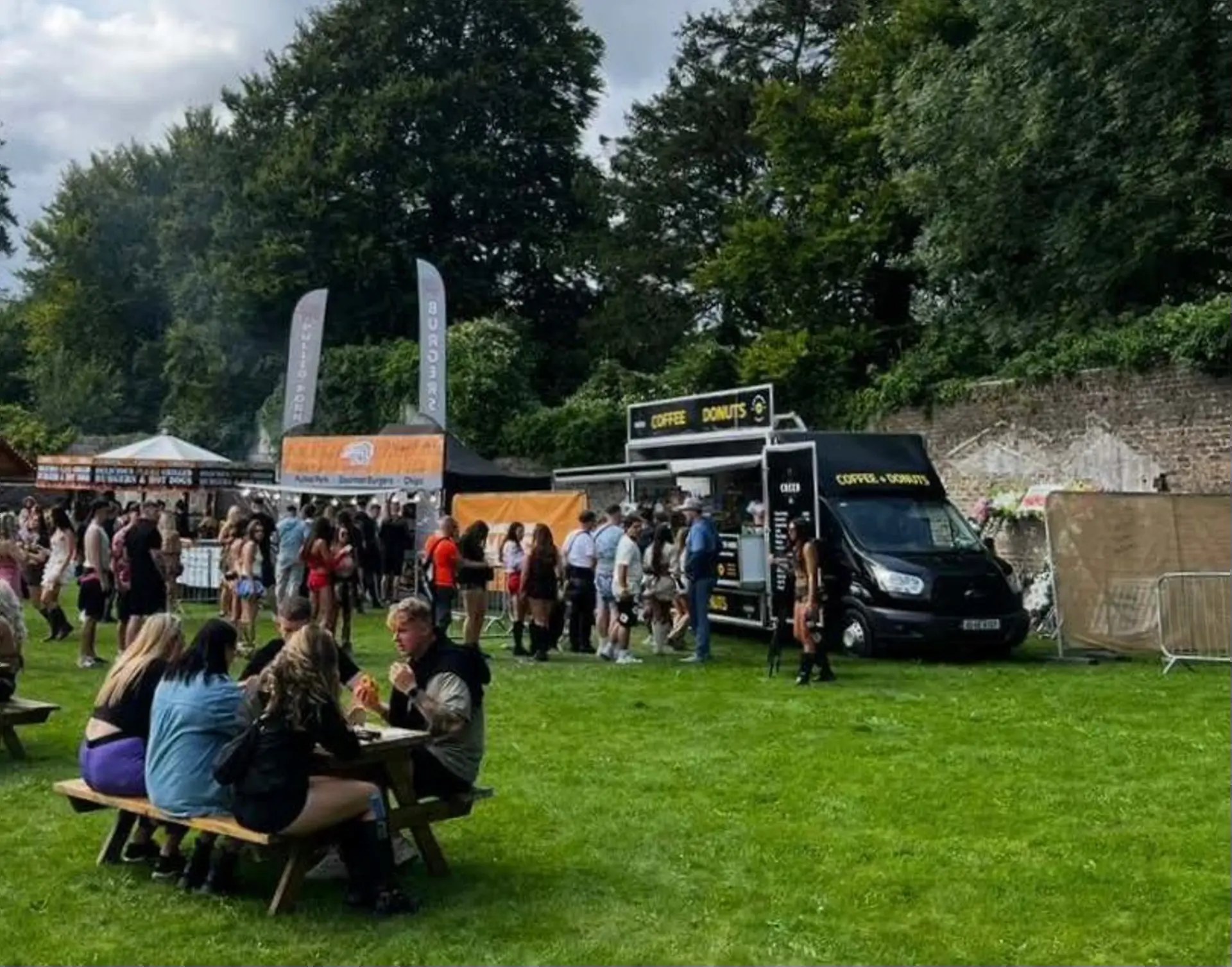 Festival crowds and picnic tables on the grass with the Coffee & Donuts van serving