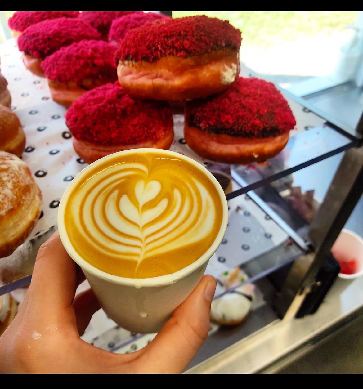 Latte with heart latte art in front of red velvet donuts